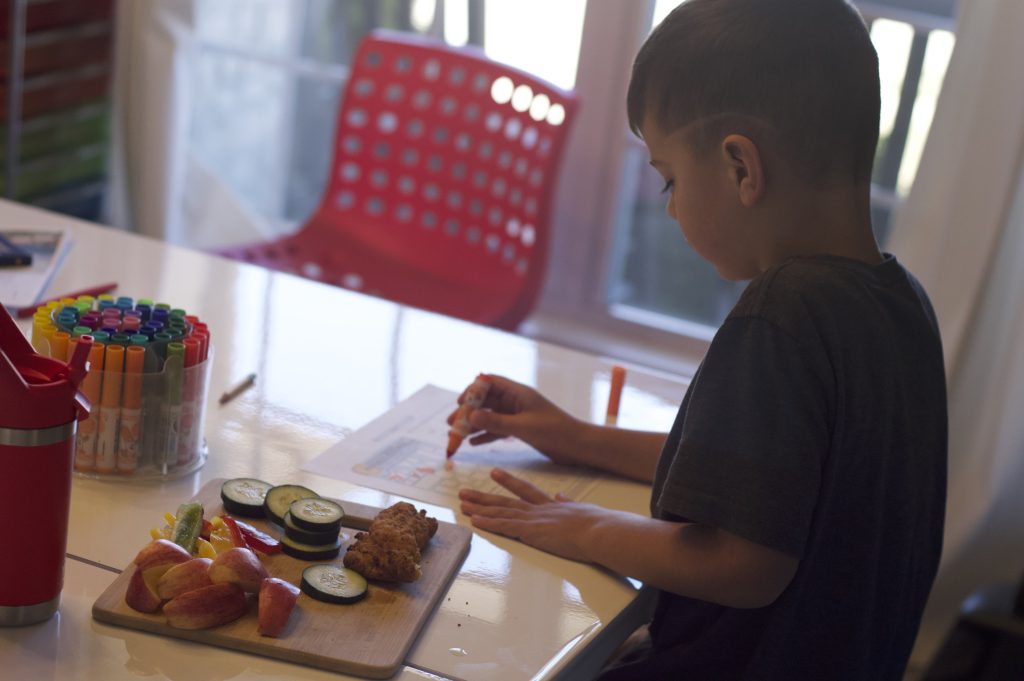 boy working on math page during homeschool time with lunch on the table