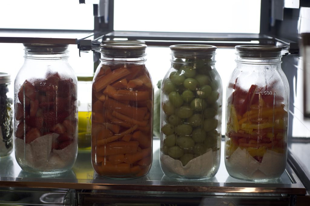 up close picture of washed and prepped produce for the week placed in large mason jars with wooden lids, organized fridge to promote healthy eating