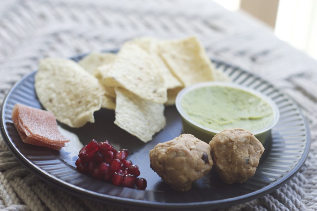 close up lunch of protein balls, pomegranate seeds, joyride, tortilla chips, guacamole